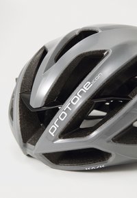Casque de vélo gris avec un design aérodynamique, de multiples trous de ventilation et un rembourrage intérieur noir. Marque visible sur le côté.