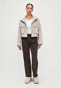 Cropped beige jacket with two chest pockets, white t-shirt underneath, brown straight-leg pants, and beige chunky sneakers.