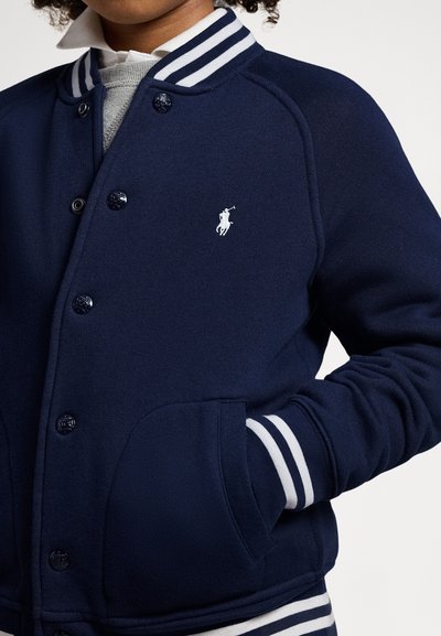 Mörkblå sweatshirtjacka med randig ribbad krage och mudd. Har runda knappar, framfickor och en vit logotyp på bröstet.