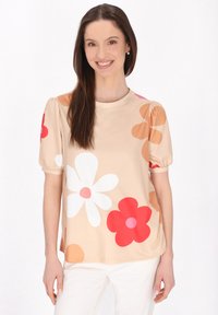 Kortærmet top i beige med overdimensionerede blomster mønstre i rød, pink og hvid. Har en rund halsudskæring og plisserede ærmer.