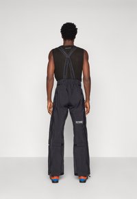 Czarne spodnie sportowe z regulowanym pasem, bocznymi kieszeniami i zamkami błyskawicznymi przy kostkach. Modelka nosi również czarny top na ramiączkach.