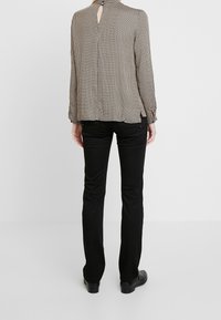 Svart och vit rutig blus med långa ärmar och en nyckelhålöppning baktill, kombinerad med svarta slim-fit byxor och platta svarta skor.