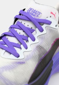 Buty biegowe Puma z białą i purpurową gradientową cholewką, teksturowanym materiałem, purpurowymi sznurowadłami i charakterystycznym wzorem w zygzak na podeszwie środkowej.