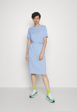 Vestido de t-shirt azul claro com mangas curtas, detalhe de cintura atada, comprimento até aos joelhos, combinado com ténis desportivos e meias verde-brilhante.