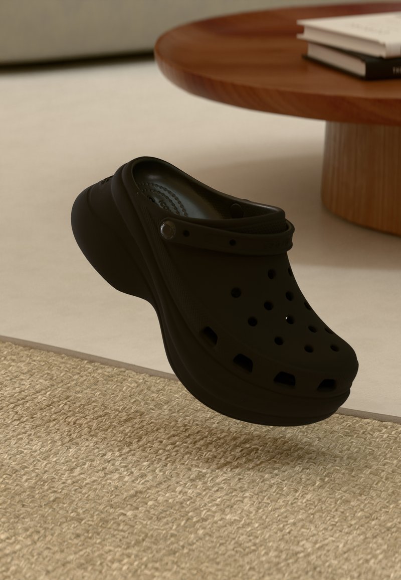 Tamanco de borracha preta com aberturas para ventilação, bico arredondado e sola resistente. Salto ligeiramente elevado, exibido sobre um tapete texturizado.