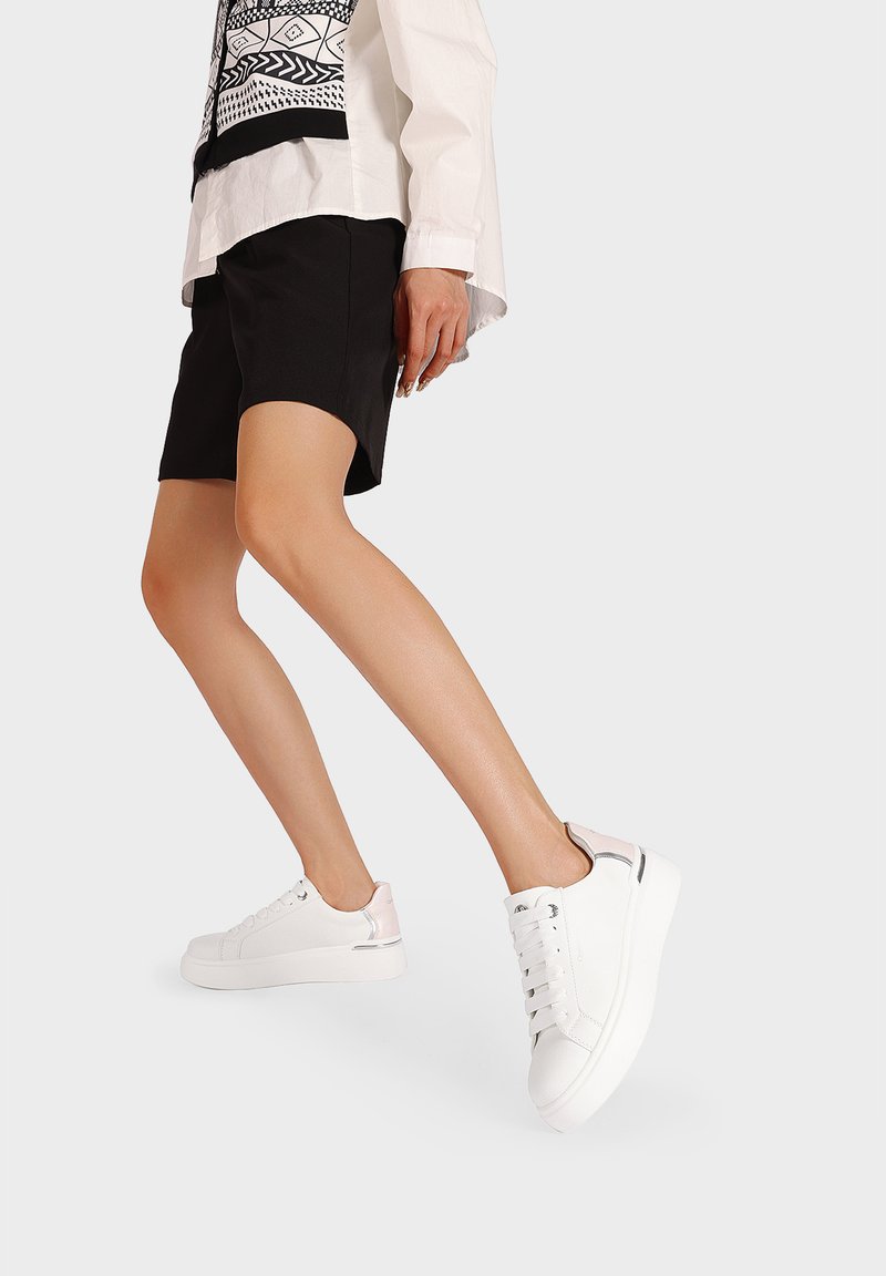 Sneaker bianchi con finitura in pelle liscia, punta tonda, chiusura con lacci e accenti metallici a contrasto sul tallone. Design semplice e contemporaneo.
