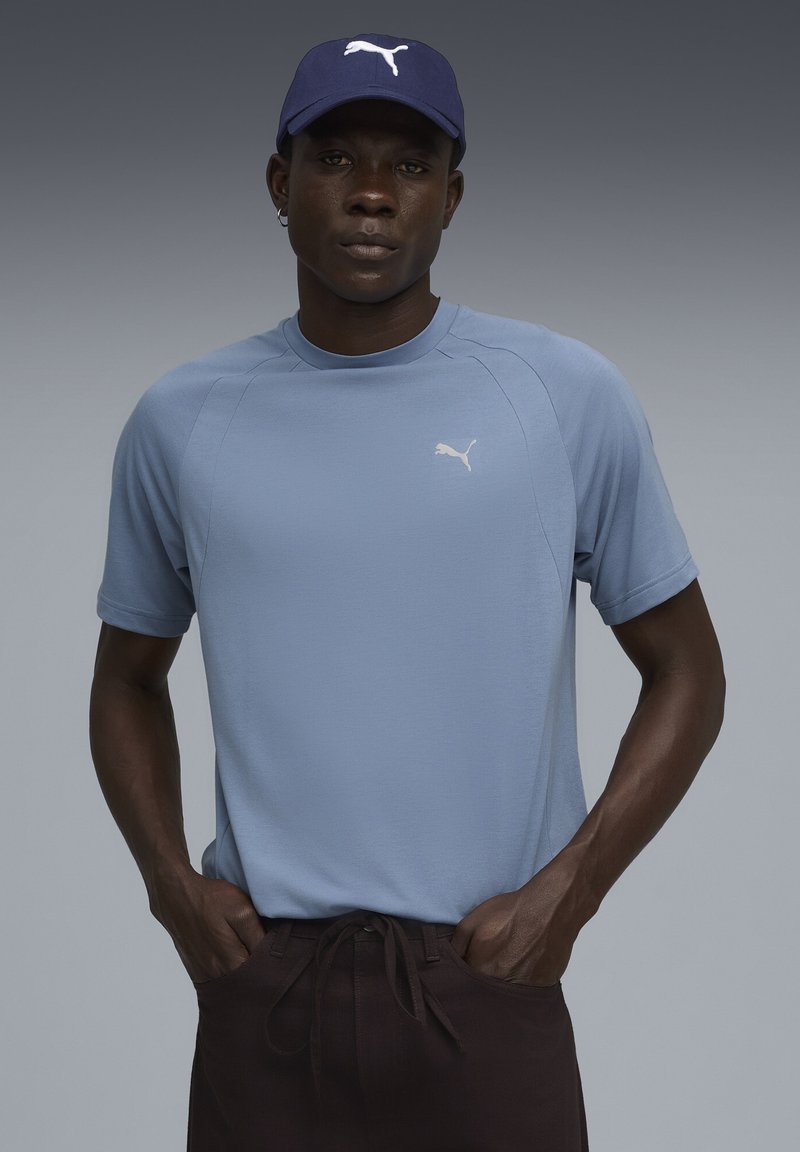 Lys blå atletisk t-shirt med korte ærmer og rund hals, prydet med et hvidt Puma-logo på brystet, parret med mørke bukser.