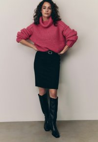 Chunky rosa stickad tröja med polo-krage, svart blyertskjol och knähöga svarta läderstövlar. Har rullade ärmar och bälte som accent.