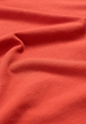 Rdeča bombažna tkanina z gladko teksturo, ki prikazuje mehke gube in nagube po vsej površini ter ujame svetlobo z rahlim sijajem.