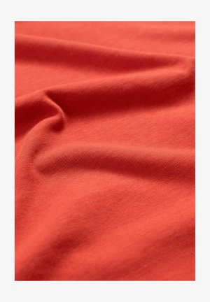 Rood katoenweefsel met een gladde textuur, dat zachte plooien en kreukels vertoont, die het licht met een lichte glans vangen.