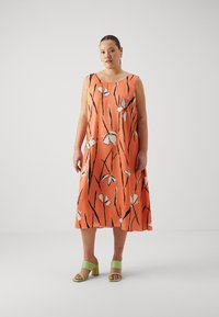 Oranje mouwloos jurkje met een zwart-wit bloemenpatroon; vloeiend ontwerp, lichtgewicht stof. Draag het met groene blokhakken.