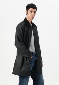 Black, lightweight, long-sleeve coat with button closure and a collar. Smooth texture, knee-length design, paired with gray shirt and denim.