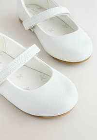 White leather Mary Jane shoes with flat soles, round toes, and a strap across the instep. Soft, textured upper and simple inner pattern.