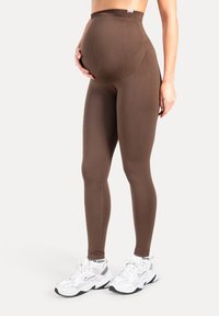 Leggings de maternité marron avec taille haute, texture lisse et coupe longue. Accompagnés de chaussures de sport blanches.