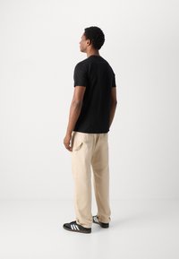 Zwarte t-shirt met korte mouwen, beige losse cargo pants, zwarte sneakers met witte strepen. Gladde stof, eenvoudig ontwerp, neutrale kleuren.