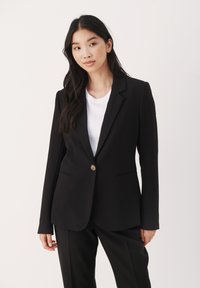 Černý blazer vyrobený z hladké tkaniny, který má jeden zlatý knoflík, klopy a dvě boční kapsy, spárovaný s bílým tričkem.