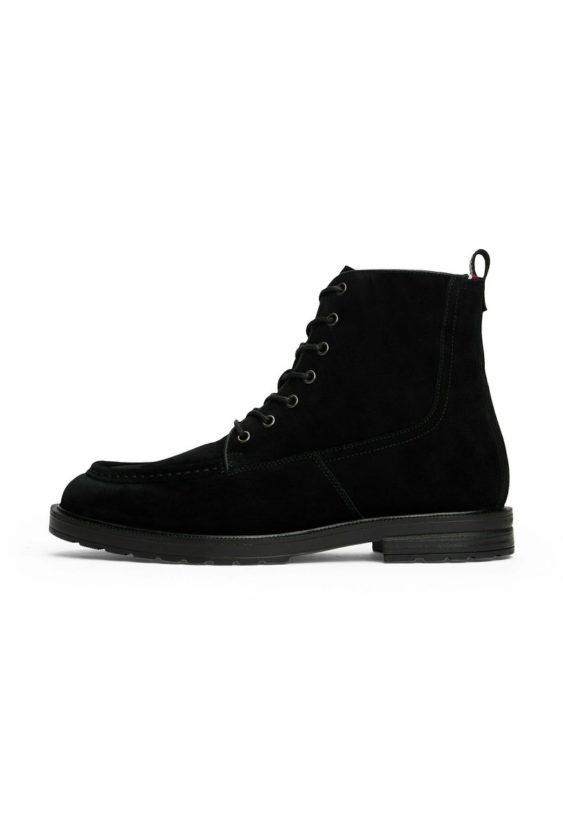 Black suede lace-up ankle boot with pull tab and low stacked heel, side view on white background.