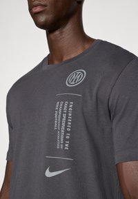 Tmavohnedé tričko s okrúhlym výstrihom, na prednej strane so symbolom Nike v bielej farbe a tlačeným textom. Krátke rukávy.