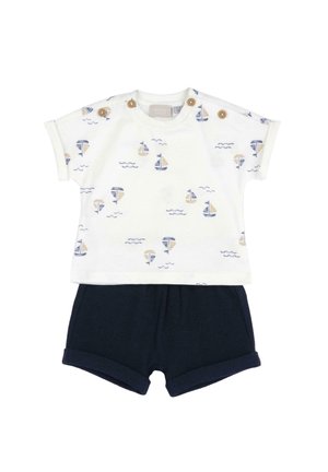 Maglietta bianca per bambino con stampe di barche a vela blu e beige e bottoni in legno sulle spalle, abbinata a pantaloncini blu scuro semplici.