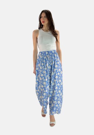 Lichte blauwe broeken met een brede pijp en bloemenpatroon, voorzien van een elastische tailleband, gecombineerd met een aansluitend wit tanktop en lichte hakken.