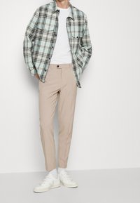 Camicia a quadri con bottoni in azzurro chiaro, grigio e nero; pantaloni beige aderenti; scarpe da ginnastica bianche con accenti neri; texture liscia.