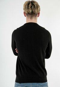 Maglione nero a maglia con scollo e polsini a coste, caratterizzato da un design aderente e una texture liscia. La vista dal retro mostra un tessuto semplice senza decorazioni.