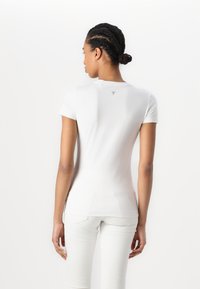 T-shirt blanc ajusté à manches courtes, en coton doux, avec un petit logo triangulaire dans le haut du dos, texture lisse et coupe contemporaine.