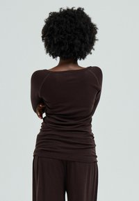 Brown long-sleeve top with a wide neckline and fitted silhouette, made of soft fabric, paired with matching loose pants.