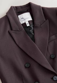 Dunkelvioletter, doppelt geknöpfter Blazer mit Reverskragen, schwarzen Knöpfen und glattem schwarzen Futter, aus strukturiertem Stoff und minimalem Branding.