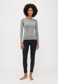 Maglietta grigia a maniche lunghe con un design aderente, abbinata a leggings neri con un motivo testurizzato. Entrambi i capi sono realizzati in un tessuto morbido e elasticizzato.