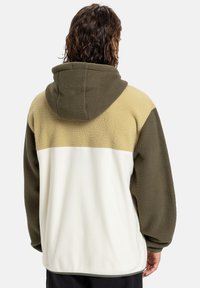 Fleecová bunda s oversized kapucí. Barevné blokování v zelené, béžové a bílé. Texturovaný povrch, volný střih a žebrované manžety.