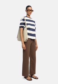 Pasiasty bawełniany t-shirt w granatowym i białym kolorze, brązowe spodnie w szerokiej nogawce oraz czarne sandały z srebrnymi akcentami; uzupełnione beżową torbą.