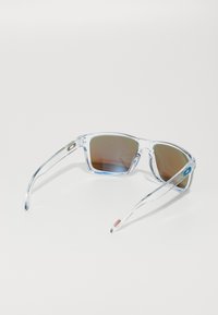 Ochelari de soare din plastic transparent cu lentile nuanțate de culoare maro, formă unghiulară, accente de marcă pe brațe și un cadru transparent cu detalii colorate.