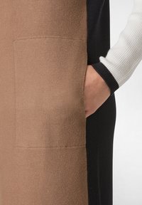 Vêtement tricoté avec un design en blocs de couleurs dans des nuances de marron, noir et crème. Comprend une poche frontale et des finitions côtelées aux manches.