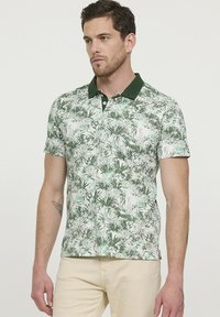 Polo shirt vert et blanc avec un motif floral, col et boutons contrastants vert foncé, manches courtes et ourlet droit.
