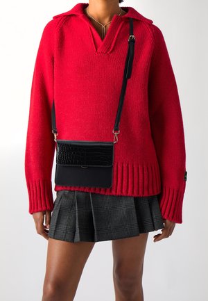 Person wearing a red knit sweater, gray plaid pleated skirt, black crossbody bag, and delicate silver necklace, shown from neck to mid-thigh.