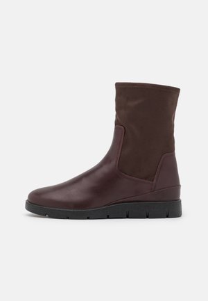 Brązowy skórzany botek za kostkę z materiałową cholewką, zaokrąglonym noskiem i teksturowanymi bokami. Posiada czarną gumową podeszwę z żłobionym wzorem zapewniającym przyczepność.