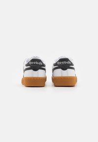 White sneakers with black accents, textured rubber soles, and logo detailing on the back. Smooth leather upper and padded collar.
