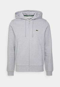 Sudadera gris con cremallera fabricada en una suave mezcla de algodón. Cuenta con capucha, mangas largas, bolsillos frontales y un pequeño logo verde de Lacoste.