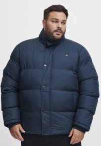 Navy blue puffer jacket with a high collar, snap buttons, quilted design, and side pockets; made from smooth, insulated material.