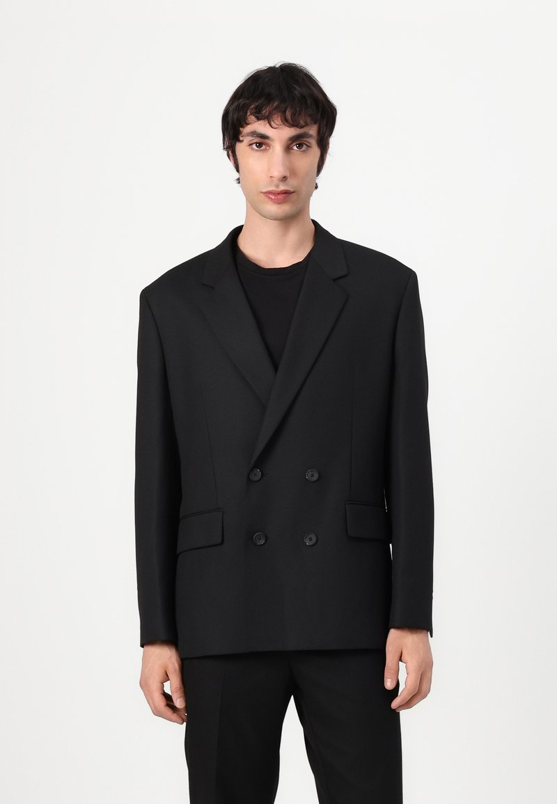 Black double-breasted blazer made of smooth fabric, featuring a notched lapel, two front pockets, and black buttons. Straight cut design.