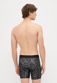 Μαύρα μποξεράκια με γεωμετρικό γκρι σχέδιο, με μαύρη ελαστική μέση που φέρει λογότυπο. Το υλικό φαίνεται λείο και εφαρμοστό.