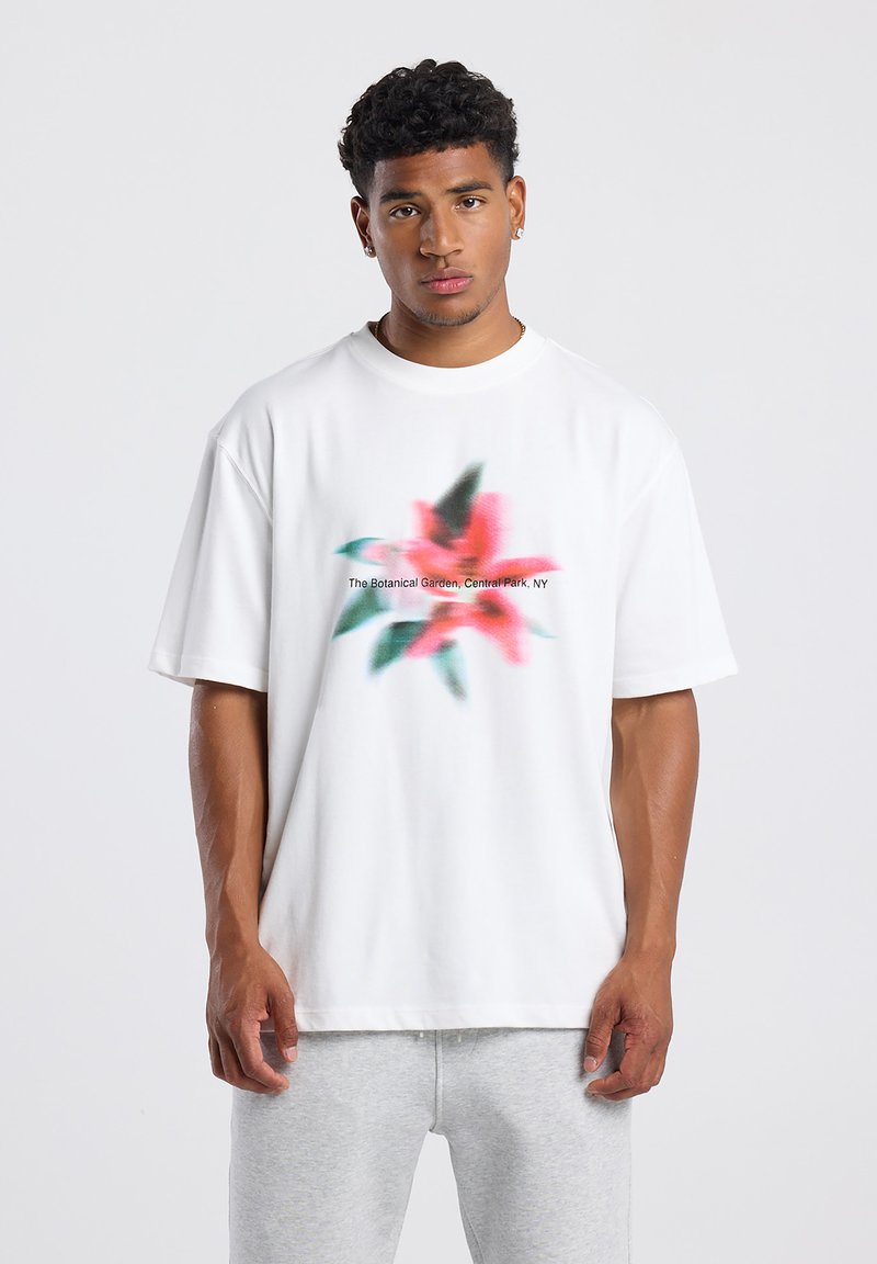 Camiseta de algodón blanca con un diseño floral difuminado en rosa y verde, con el texto "El Jardín Botánico, Central Park, NY" impreso.