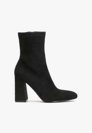 Črne antilop čevlje do gležnjev s koničastim nosom, blokastim peto in gladko teksturo. Imajo visoko škatlo in minimalno šivanje.