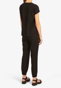 Abito due pezzi nero composto da una maglietta a maniche corte e pantaloni affusolati con polsini elasticizzati. Il tessuto appare liscio, con un design semplice.