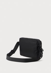 Černá obdélníková ramenní taška vyrobená z hladké tkaniny, s zipovým uzávěrem a odnímatelným, nastavitelným popruhem.