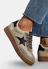 Baskets en daim beige avec un design d'étoile noire, des accents scintillants sur l'orteil et des lacets en imprimé léopard. Dotées d'une semelle en caoutchouc brun et de languettes noires au talon.