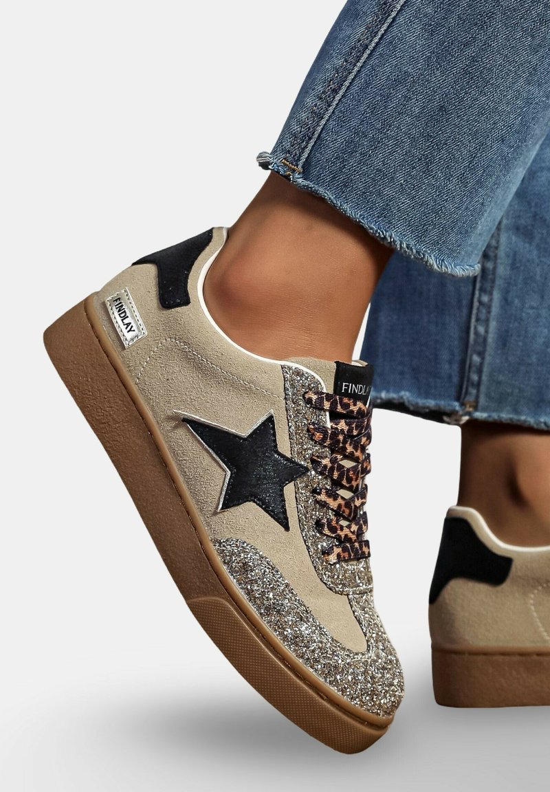 Baskets en daim beige avec un design d'étoile noire, des accents scintillants sur l'orteil et des lacets en imprimé léopard. Dotées d'une semelle en caoutchouc brun et de languettes noires au talon.