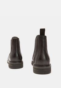 Cizme negre din piele, de gleznă, cu o textură netedă, panouri laterale elastice, buclă de prindere și tălpi din cauciuc stratificat. Design simplu și elegant.