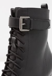 Botas de cuero negras hasta el tobillo con parte delantera con cordones, detalle de hebilla lateral, superficie texturizada y acabado liso, con costuras reforzadas.